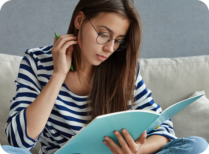 pretty-student-with-dark-hair-focused-textbook-sits-crossed-legs-sofa 1